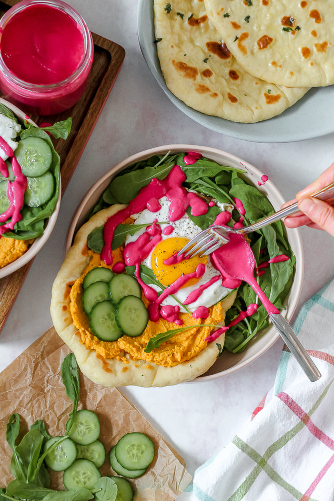 Smokey Roasted Carrot Hummus Naan with Fried Eggs, Arugula, and Beet Tahini